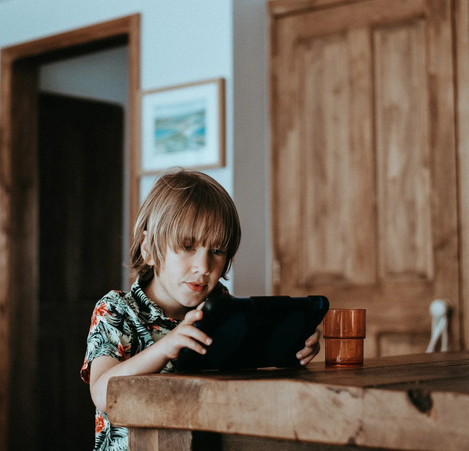 A young child absorbed in a tablet screen at a kitchen table